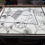 Bottom half of the stained glass design cut out of black plastic - glued to clear cast acrylic sheet - on light table ready to be painted